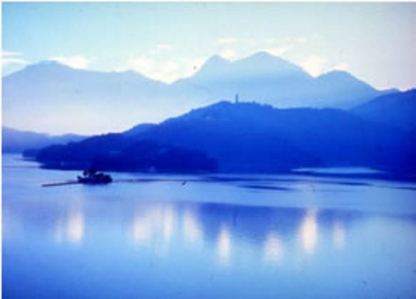 A bluish-cast photo of Sun Moon Lake, with mountains in the background.