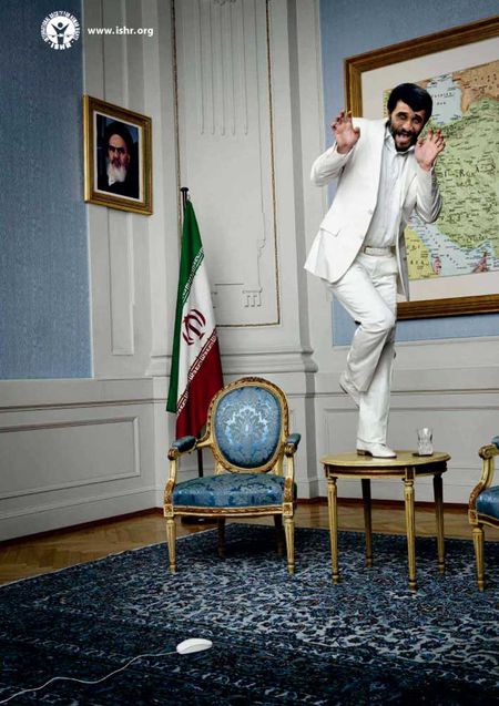 Mahmoud Ahmadinejad in white suit standing on a small, round table like a woman in a 60s sitcom, terrified of a computer mouse on the floor.