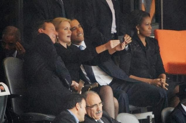 British Prime Minister David Cameron, Danish Prime Minister Helle-Thorning Schmidt and U.S. President Barack Obama take selfie at Nelson Mandela's funeral. Michelle Obama sits apart, unamused.